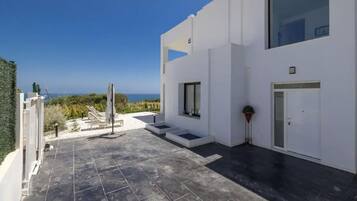 A modern building with a flat roof, a small outdoor seating area with chairs and a table, and a view of the sea.