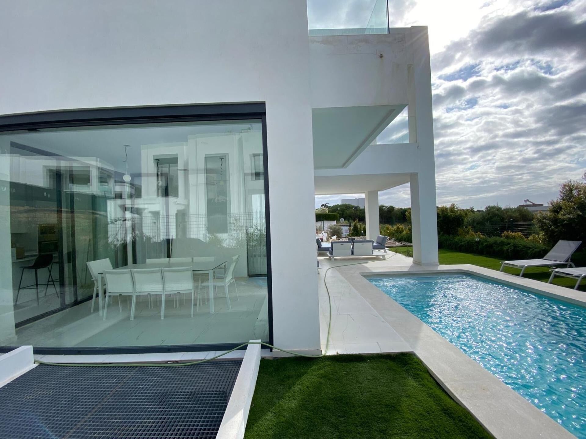 Une maison moderne dotée d’une salle à manger entièrement vitrée, d’une piscine et d’un patio avec des chaises longues.