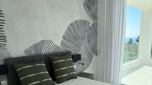 Un dormitorio moderno con una cama grande, mesitas de noche verde oscuro y vistas al océano desde un balcón.