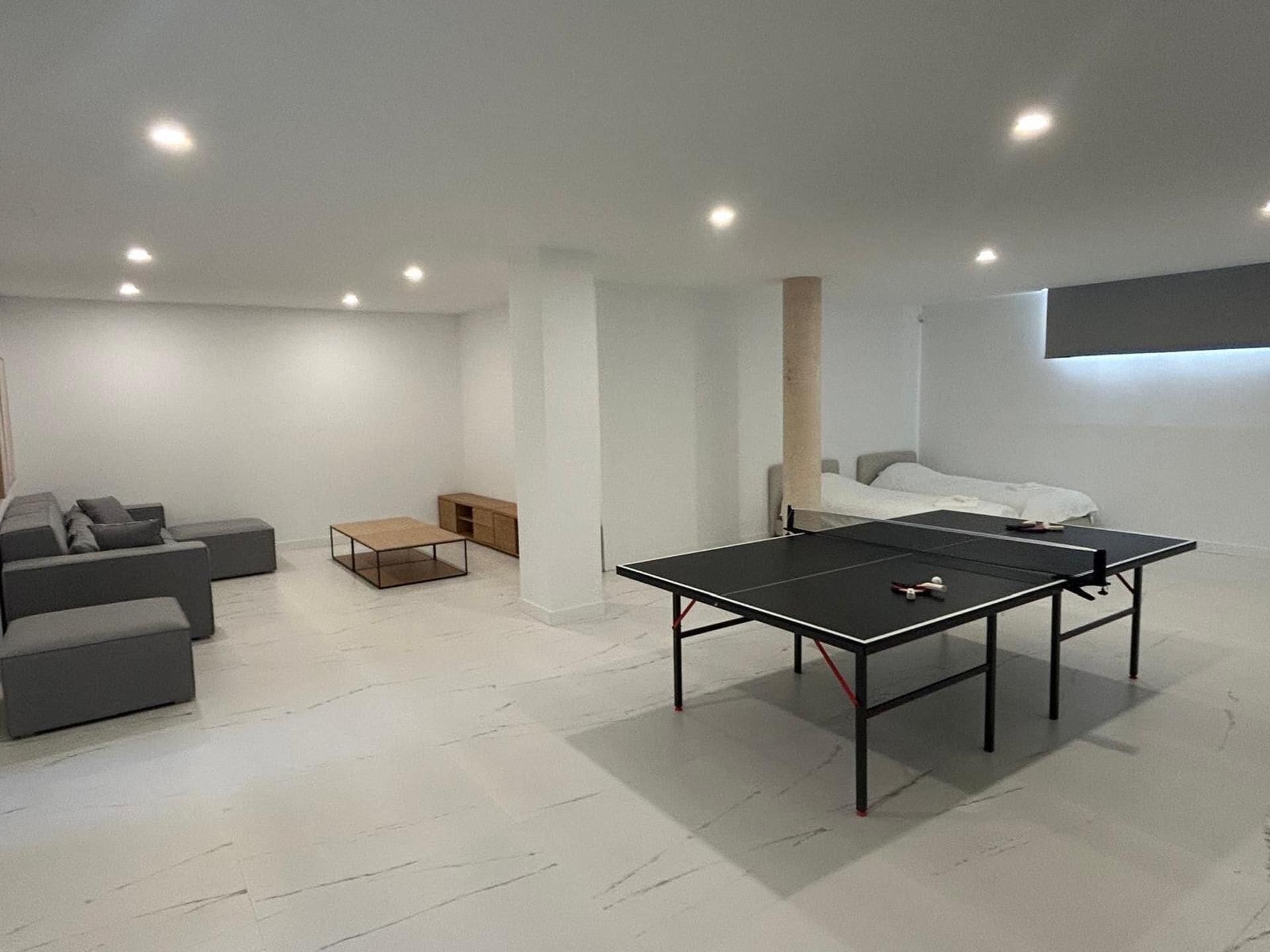 A modern living room with a ping pong table, a sofa, a coffee table, and a bed.
