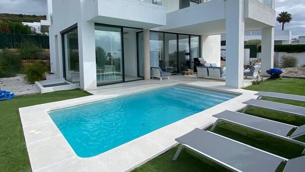 Una casa moderna de dos pisos con piscina, mobiliario exterior y un césped bien cuidado.