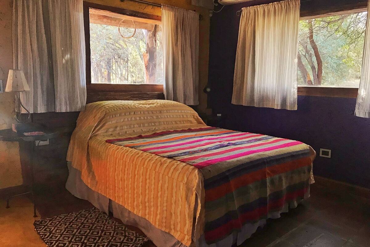 A bedroom with a bed, a bedside table, a lamp, and a window with curtains.