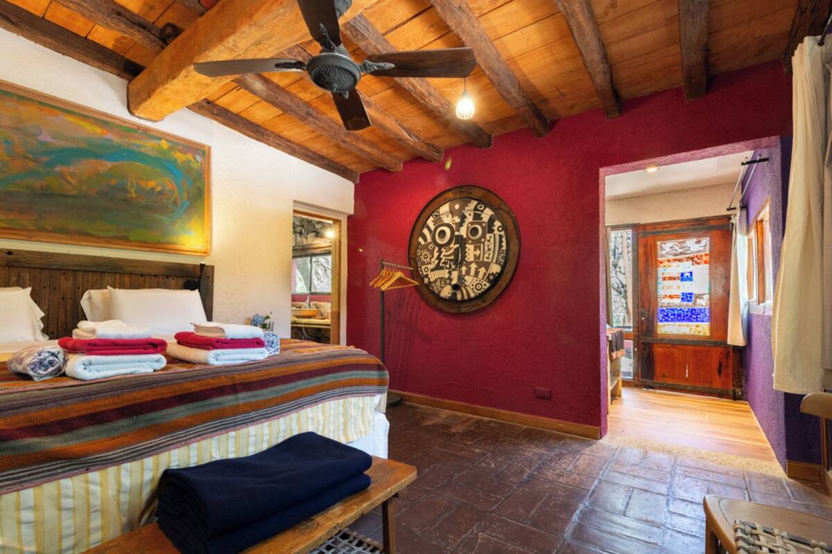 A room with a bed, a ceiling fan, a red wall, and a door leading to another room.