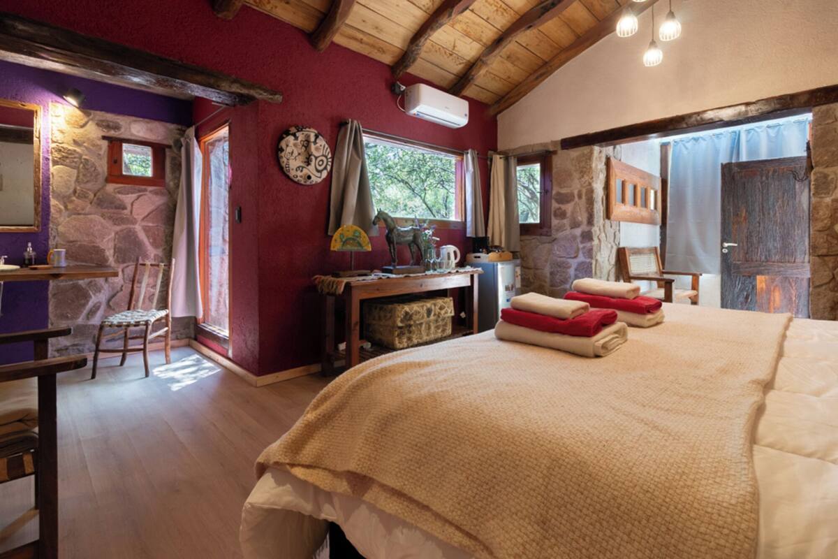 A room with a bed, a table, a chair, a fireplace, and a stone wall.