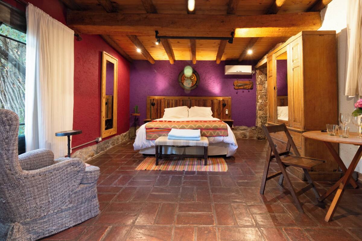 A bedroom with a bed, a chair, a table, and a stone wall.