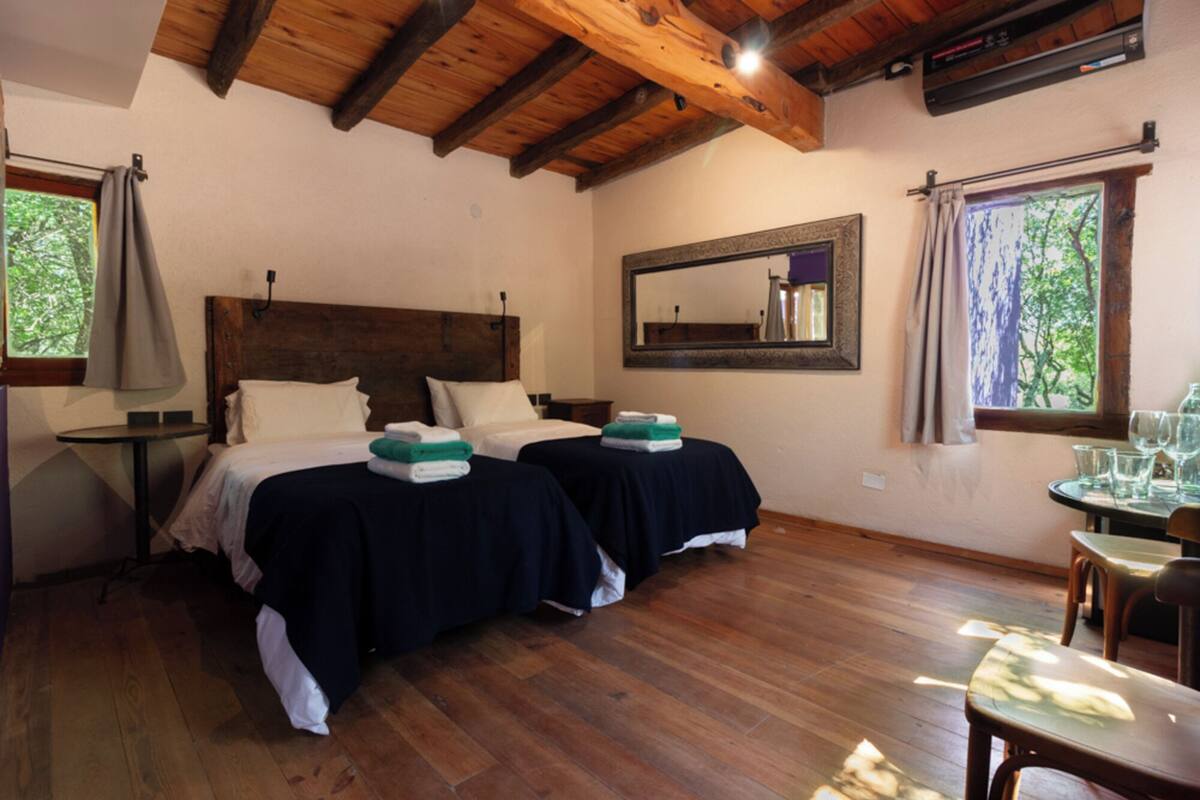 A room with two beds, a wooden ceiling, a mirror, and a window with curtains.