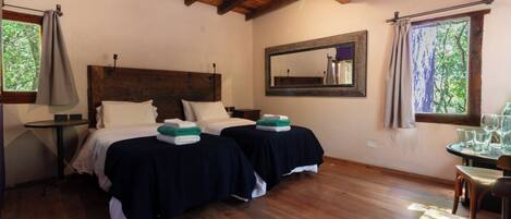 A room with two beds, a wooden ceiling, a mirror, and a window with curtains.
