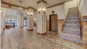 Un vestíbulo de hotel con suelo estampado, columnas decorativas, apliques de pared y una escalera con baldosas estampadas.