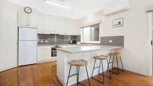 Eine moderne Küche mit weißen Schränken, einem eingebauten Backofen, einer großen Kochinsel mit Hockern und einem Fenster über der Spüle.