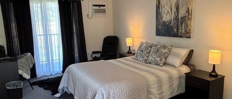A hotel room with a bed, two bedside tables with lamps, a chair, a desk, a trash bin, and a window with curtains.