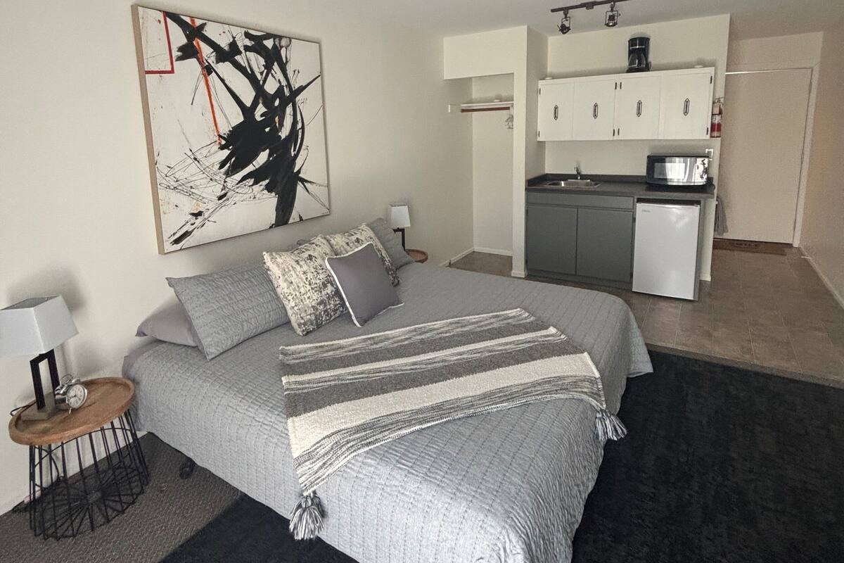 A bedroom with a bed, bedside table, lamp, and a painting.