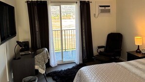 Ett hotellrum med en säng, ett skrivbord, en stol, en tv, en lampa och ett fönster med gardiner.