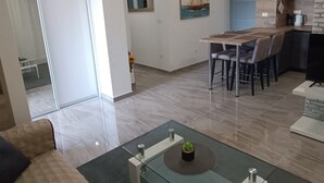Una sala de estar moderna con una mesa de centro de vidrio, una zona de comedor con una mesa y sillas de madera, una cocina con estufa y un amplio ventanal.