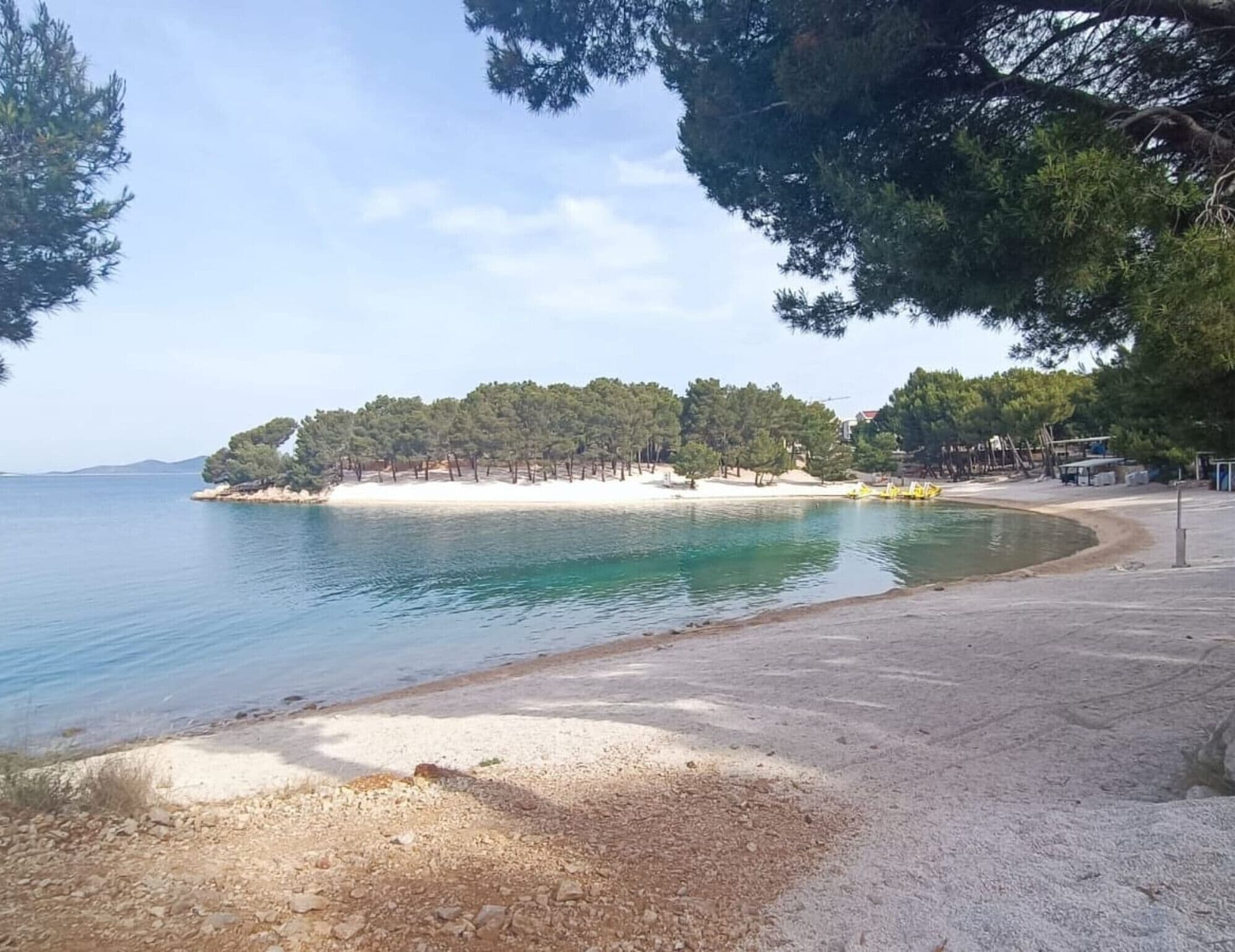 Una playa con arena, una pequeña isla con árboles y agua tranquila.
