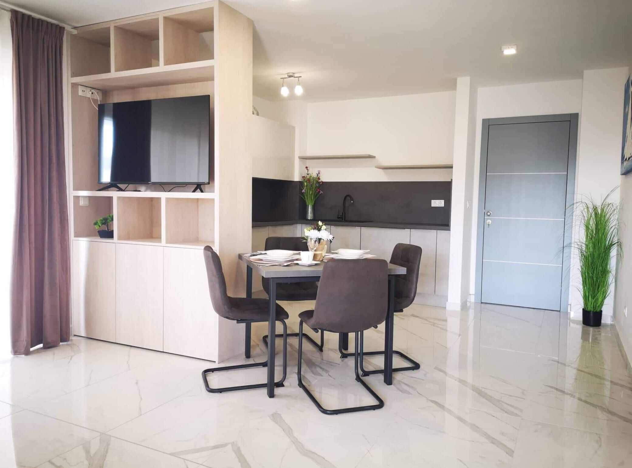 Un salon moderne comprenant un coin repas, un téléviseur fixé au mur, un espace cuisine et une porte.