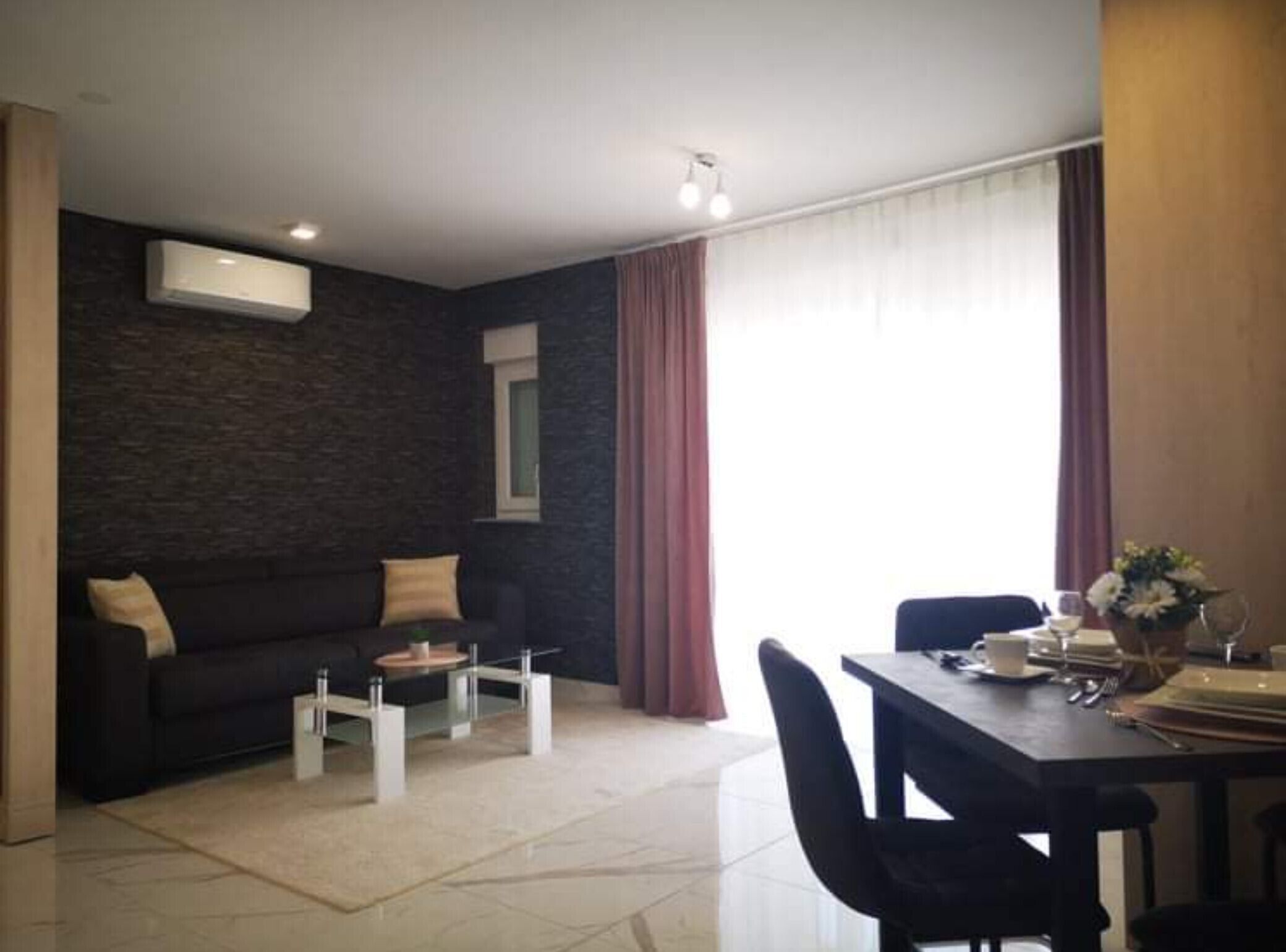 A modern living room with a dark textured wall, a sofa, a coffee table, and a dining area with a table set for two.