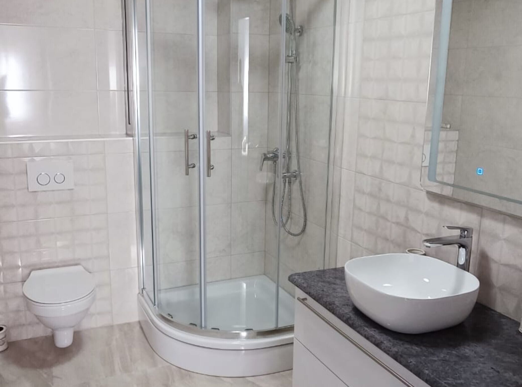 A modern bathroom with a glass-enclosed shower, a white sink, and a toilet.