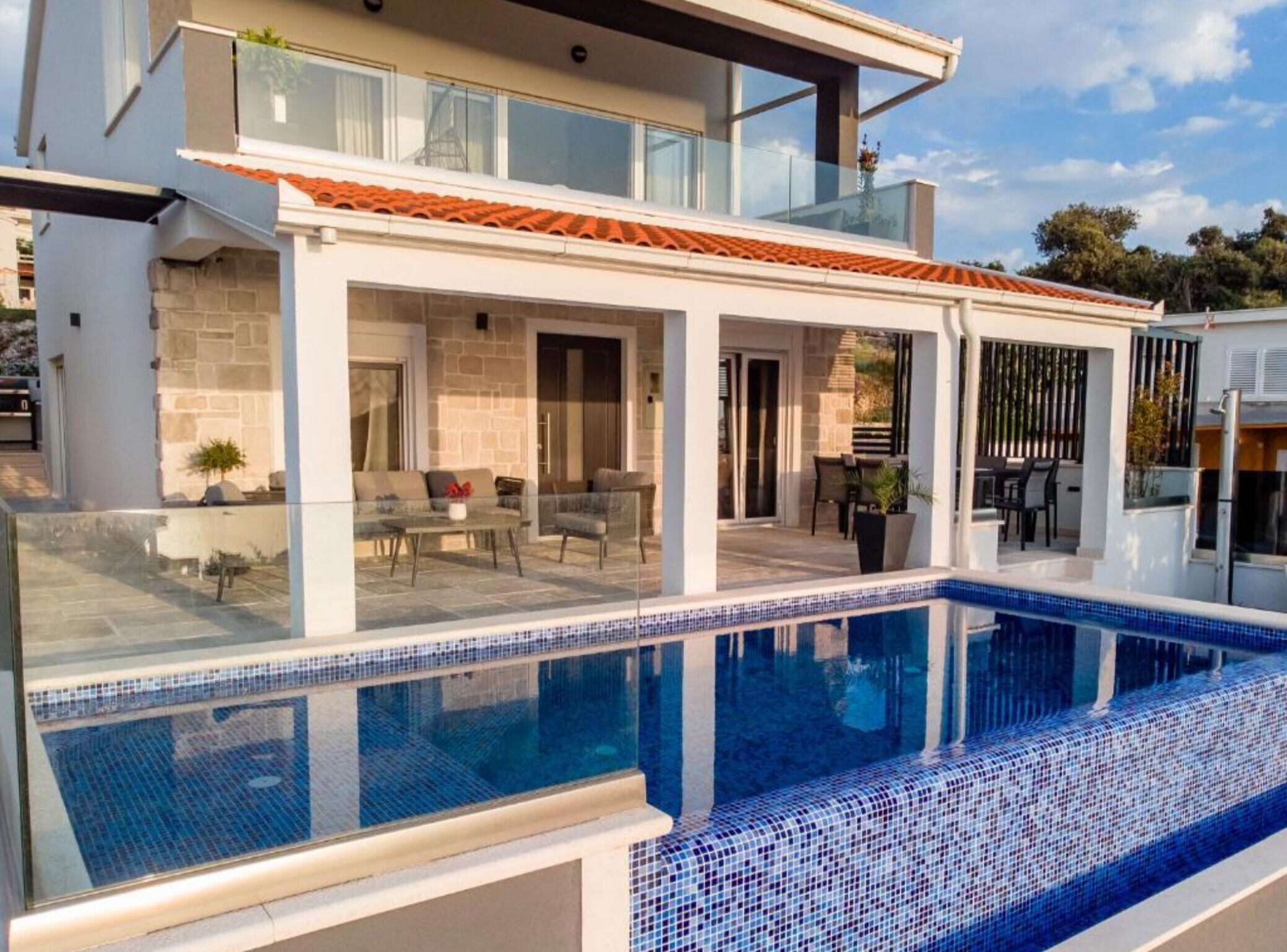 Una casa moderna de dos pisos con piscina, mobiliario exterior y fachada de piedra.