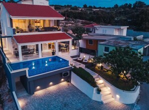 Ein modernes, zweistöckiges Haus mit Schwimmbad, Sitzgelegenheiten im Freien und einem angelegten Garten.