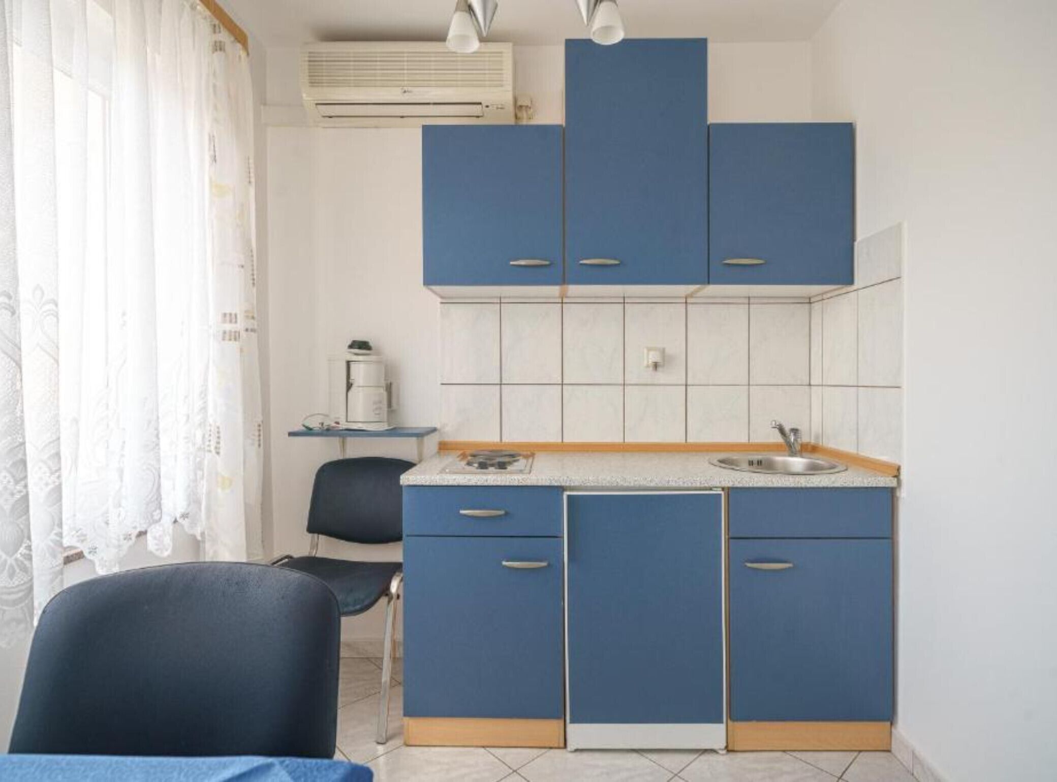 A compact kitchen with blue cabinets, a sink, and a coffee machine.