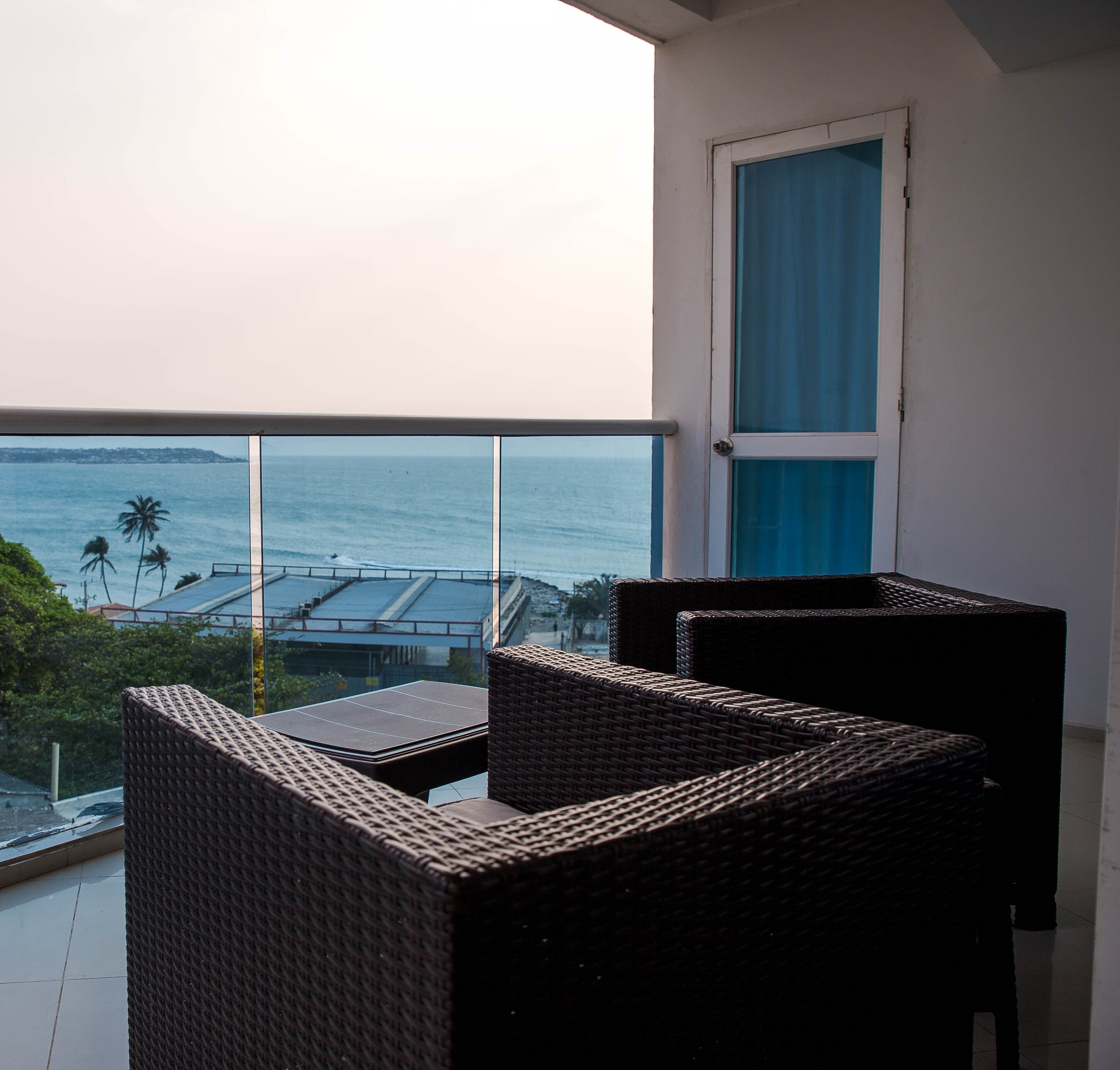 A balcony with wicker furniture, a view of the sea, and a door with blue curtains.