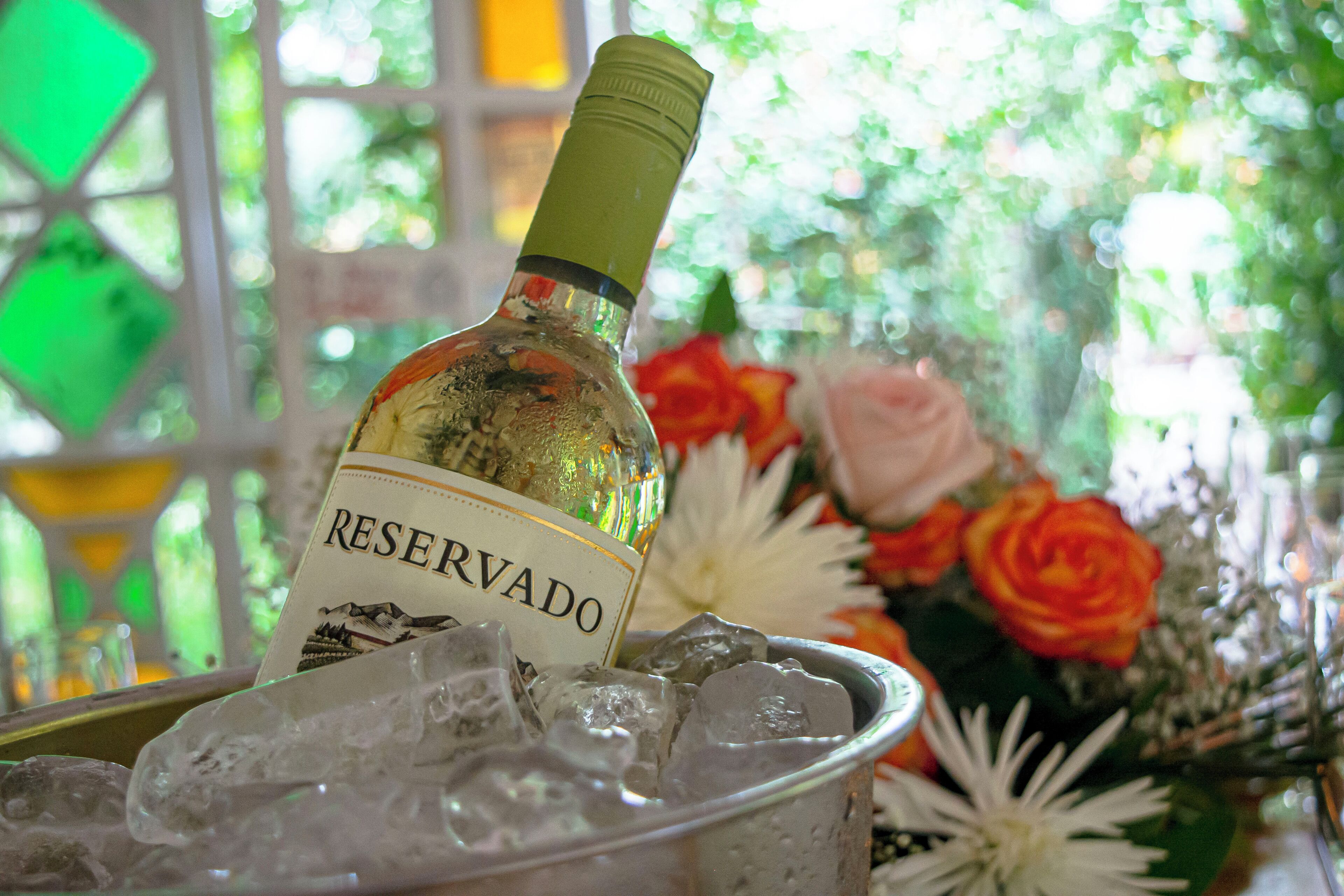Una botella de vino en un recipiente de vidrio con hielo, rodeado de flores.