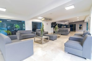 Una sala de estar moderna con sofás grises, una mesa de centro de vidrio y una cocina al fondo.