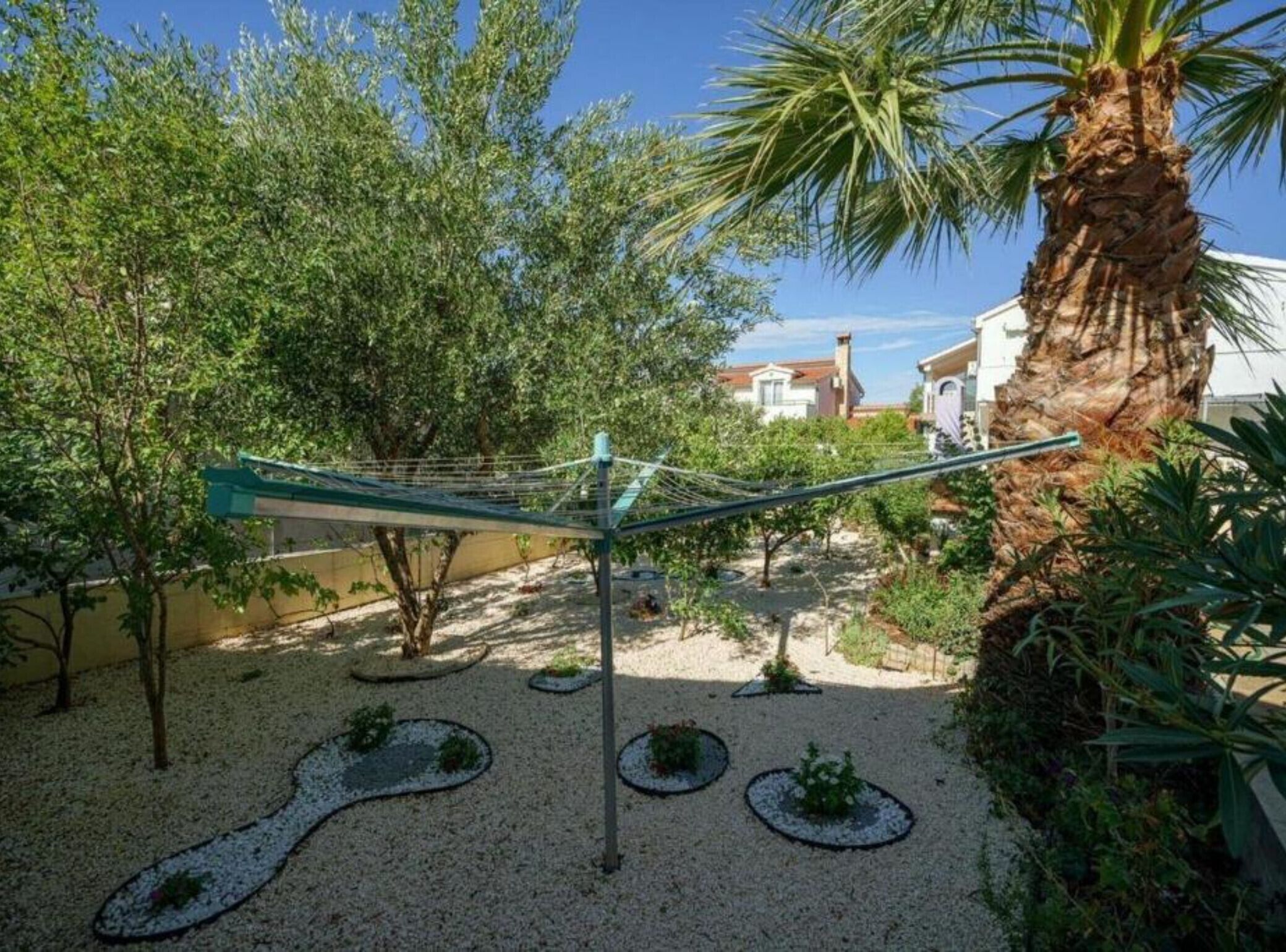 Un hamac suspendu entre deux arbres dans un jardin, avec un palmier et un bâtiment en arrière-plan.