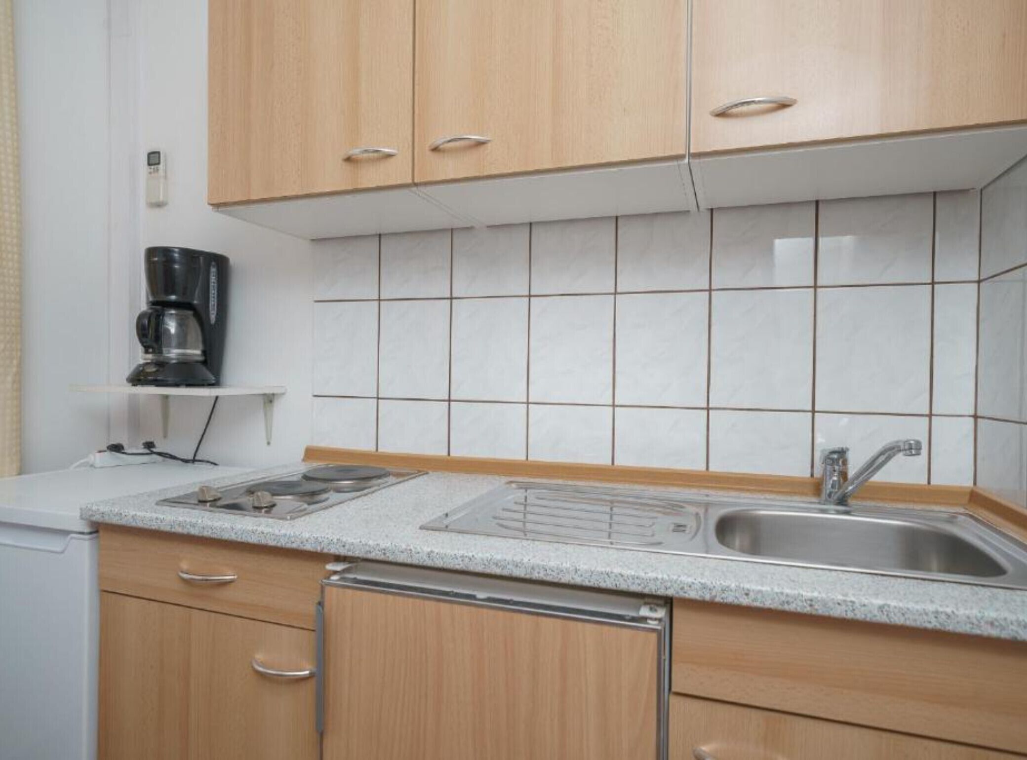 Una cocina con armarios de madera, un lavamanos de acero inoxidable, una cafetera y salpicadero de azulejos.