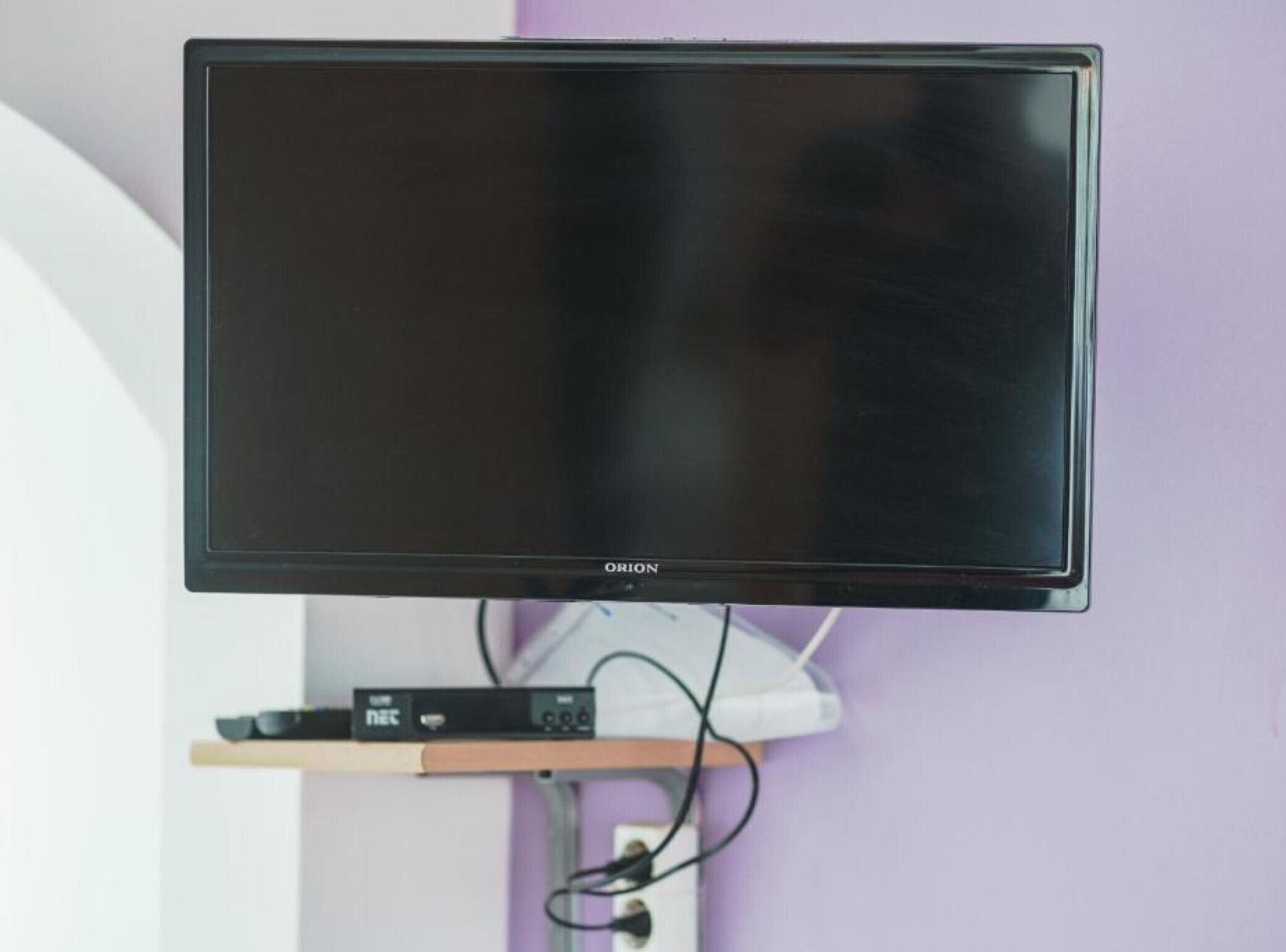 Seinälle asennettu litteänäyttöinen televisio, jonka alla on kaapelivastaanotin.