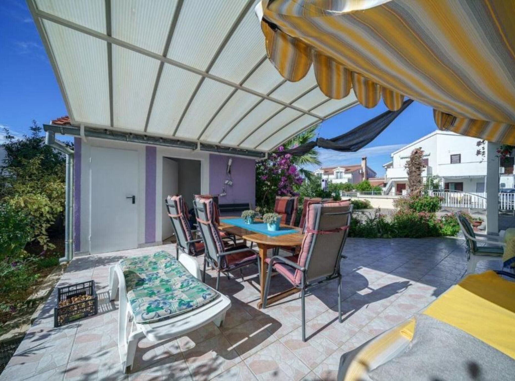 Une terrasse extérieure avec une table et des chaises, un espace salon abrité et une vue sur le quartier environnant.