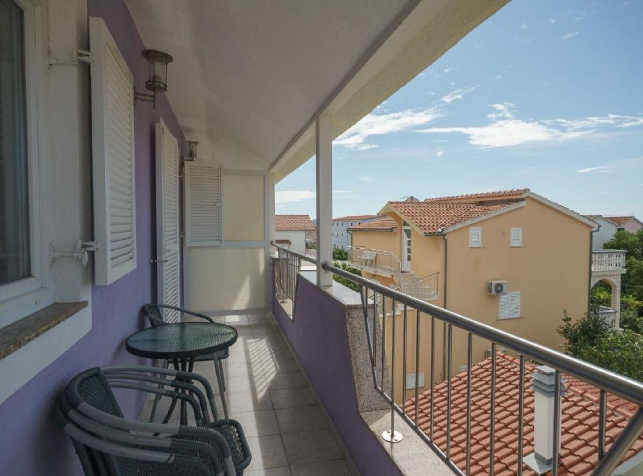 Un balcon avec une table et des chaises, une vue sur les bâtiments voisins et un ciel dégagé.
