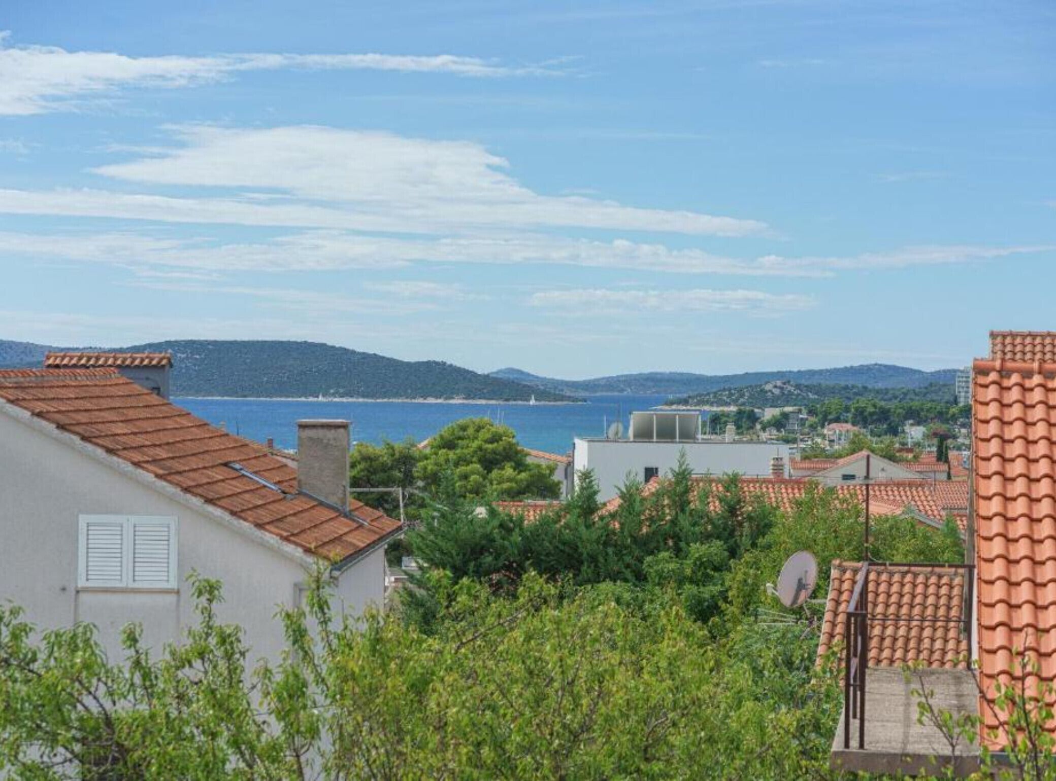 A coastal residential area with terracotta roofs, a clear sky, and a view of the sea.