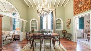 Une salle à manger avec un lustre, une table à manger en bois, des chaises et un tapis à motifs.