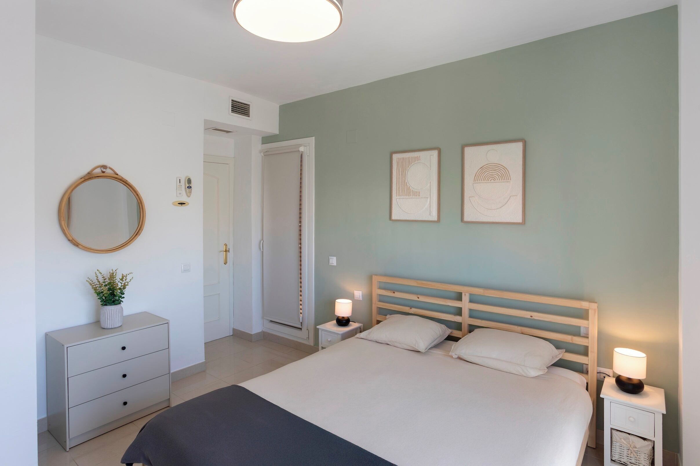 Une chambre à coucher comprenant un lit, des tables de chevet, une commode, un miroir et des œuvres d’art murales.