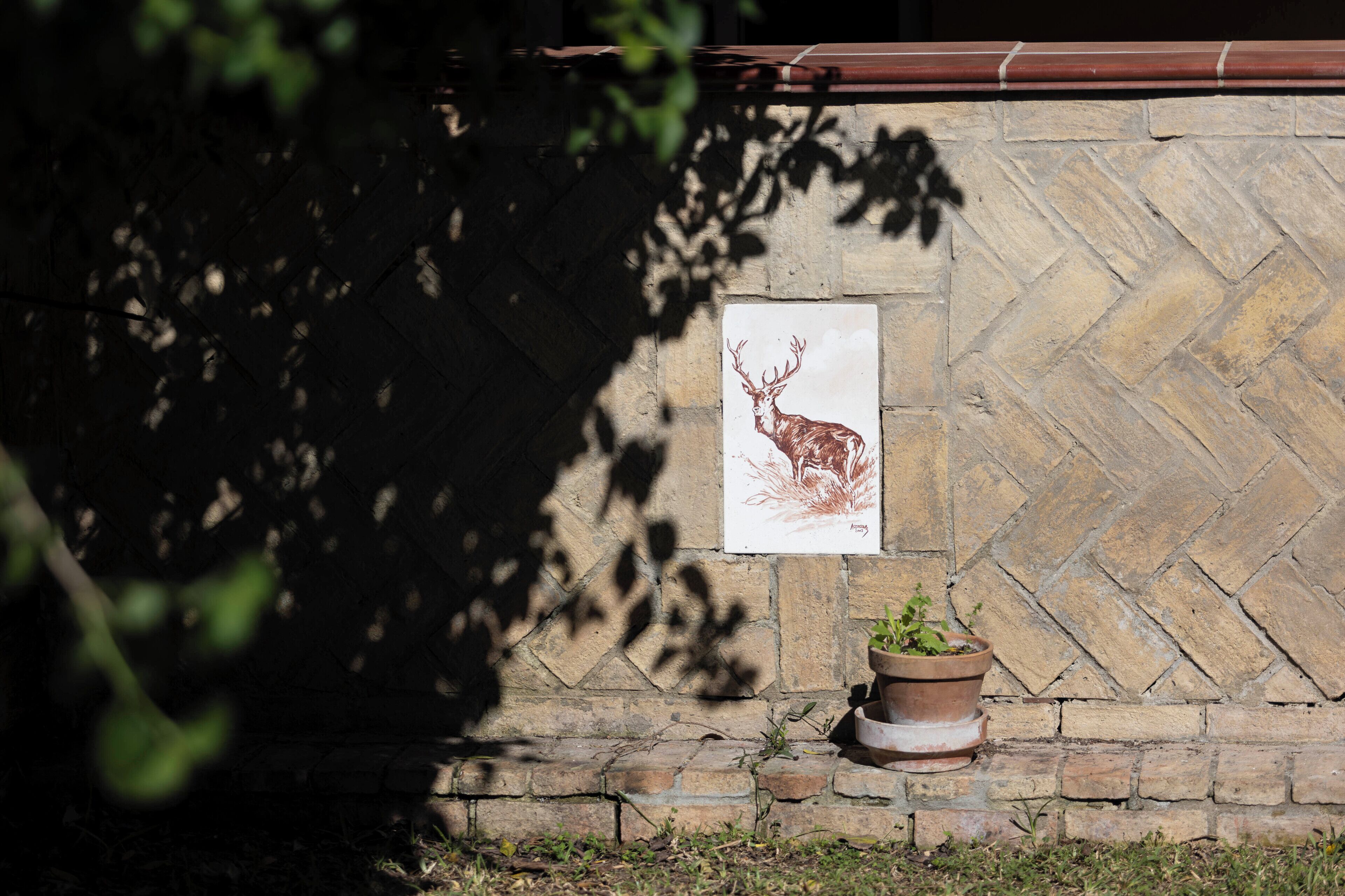 Un mur de pierres surmonté d’une illustration encadrée représentant un cerf, un pot de fleurs et une base en briques.
