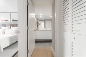 Ein Flur, der zu einem Schlafzimmer mit Bett, einem Badezimmer mit Spiegel und einer Küchenzeile führt.