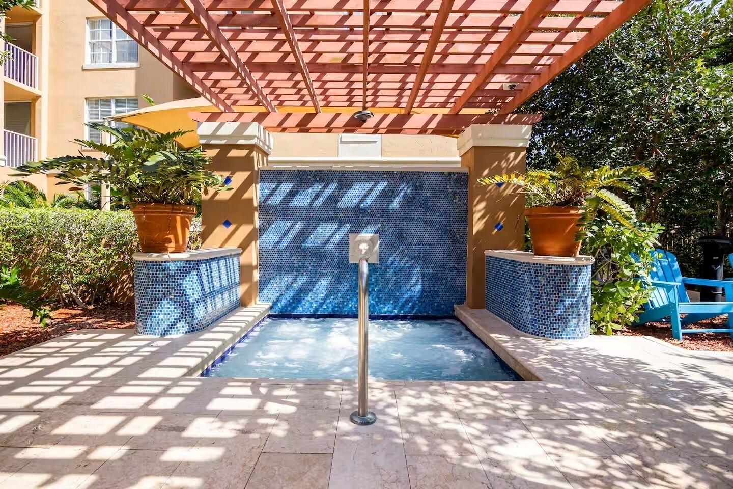 A pool area with a tiled wall, potted plants, and a pergola structure.
