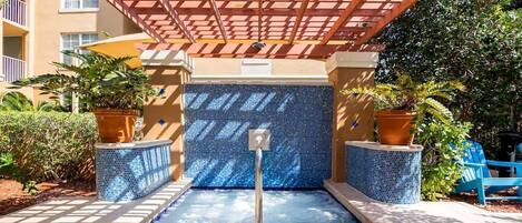 A pool area with a tiled wall, potted plants, and a pergola structure.