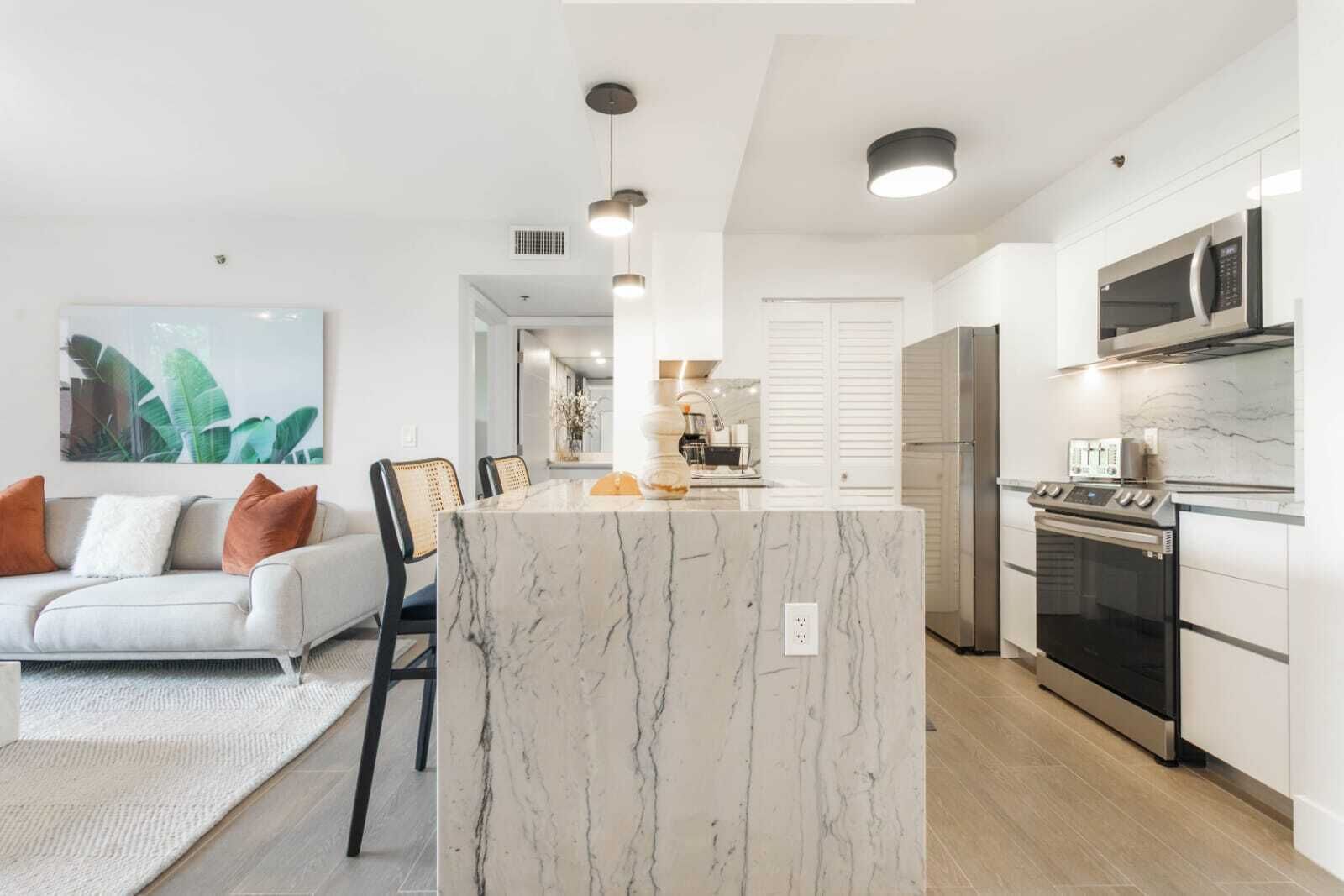 Une cuisine moderne dotée d’un îlot central, de meubles blancs, d’appareils électroménagers en acier inoxydable et d’un coin repas avec un canapé et des chaises.