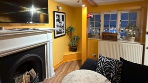 A living room with a fireplace, a television, a round table, and a window with a view of the city at night. - Cozy flat in the heart of the Lanes, with a game room and space up to 4 people (Brighton and Hove)