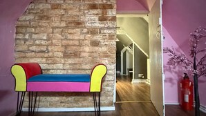 A room with a brick wall, a colorful bench, a wooden floor, and a pink wall. - Cozy flat in the heart of the Lanes, with a game room and space up to 4 people (Brighton and Hove)