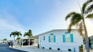 A single-story building with a white exterior and blue shutters, surrounded by palm trees and a clear sky. - Waterfront Gulf Access Home - Dock, Hot Tub, Sunset Views (Saint James City)