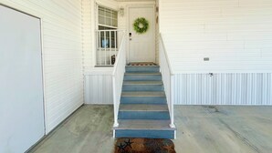 A staircase leading to a door with a wreath, white exterior walls, and a concrete floor. - Waterfront Gulf Access Home - Dock, Hot Tub, Sunset Views (Saint James City)
