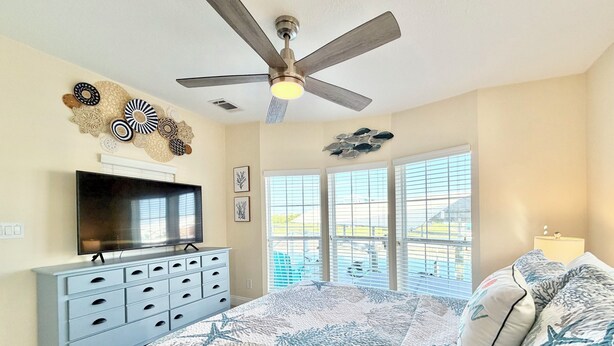 A bedroom with a large bed, a ceiling fan, a TV, and a window with blinds. - Waterfront Gulf Access Home - Dock, Hot Tub, Sunset Views (Saint James City)