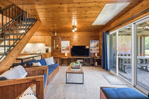 A wooden interior with a staircase, sofa, coffee table, TV, and large windows.