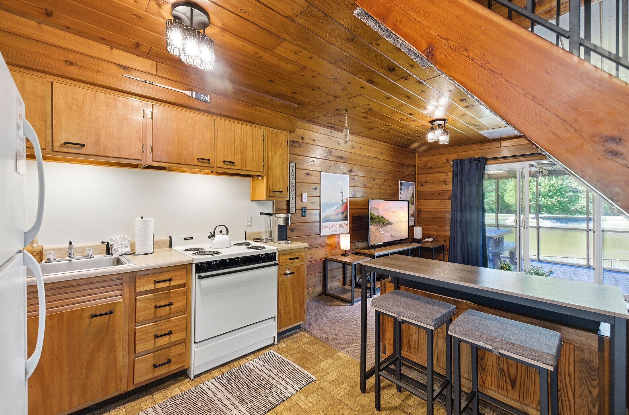 A kitchen with wooden cabinets, a stove, a sink, and a bar area with stools.