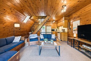 A cabin interior with a wooden interior, a sofa, a coffee table, a TV, and a staircase.