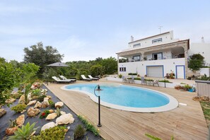 Una piscina amb gandules, una terrassa de fusta i un edifici blanc amb detalls blaus.