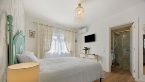 Ett sovrum med en säng, ett nattduksbord, en lampa, en tv och en dörr till badrummet.